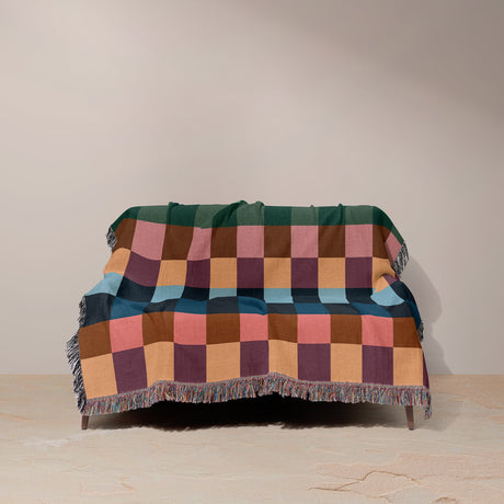 Multicolored checkered blanket draped over a chair against a plain background