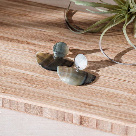 Pair of earrings on a wooden surface with a plant in the background
