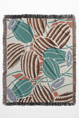 Desert-inspired woven throw blanket with cactus and floral patterns in earthy green, brown, and beige.
