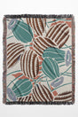 Desert-inspired woven throw blanket with cactus and floral patterns in earthy green, brown, and beige.
