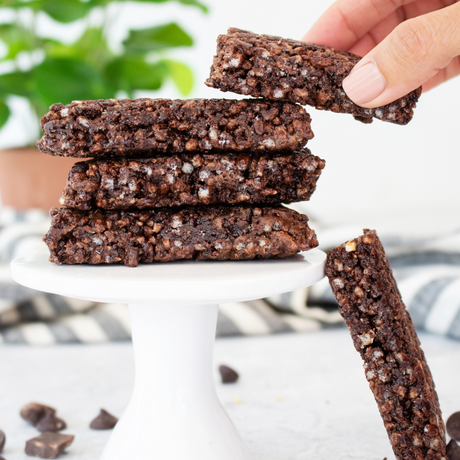 Stack of chocolate bars with a hand holding one above them on a white stand.