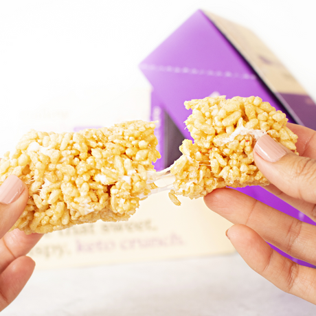 Hand holding a Rice Krispies treat with a purple box in the background