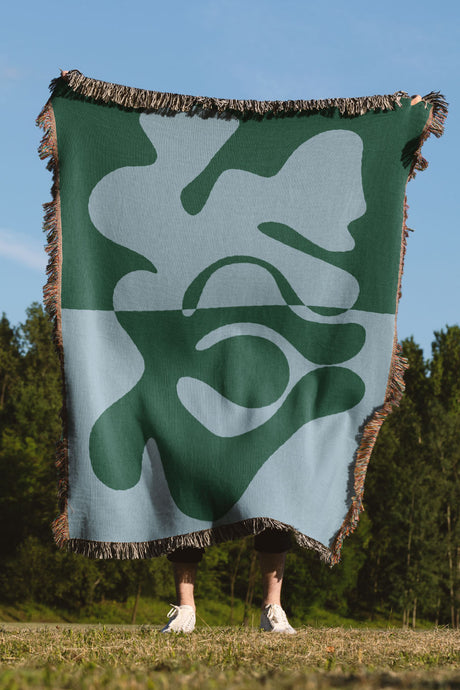 Cotton tapestry throw blanket in deep green and muted blue, finished with colorful fringe.
