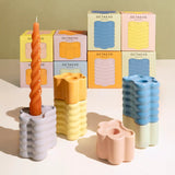 Colorful candles and candle holders with Octaevo packaging on a reflective surface.