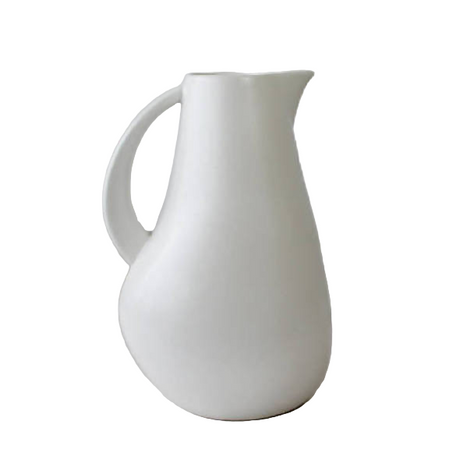 White ceramic pitcher on a light gray surface with a plain background
