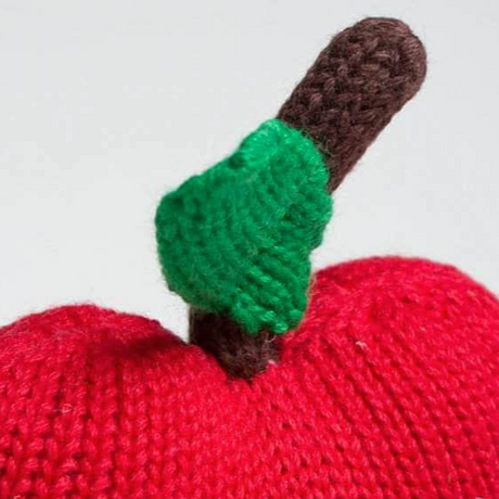 Knitted red apple with a green leaf and brown stem on a white background