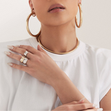 Person wearing gold hoop earrings and necklaces with a white top