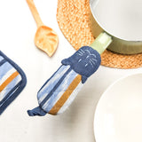 Striped oven mitt with cat design on a kitchen counter with pots and a spoon.