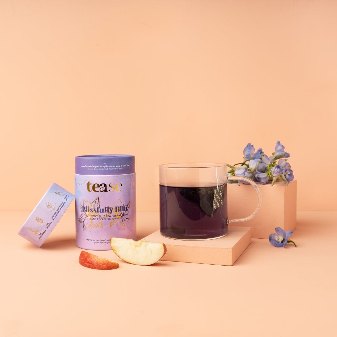 Tea packaging with a glass mug of tea, apple slices, and flowers on a peach background