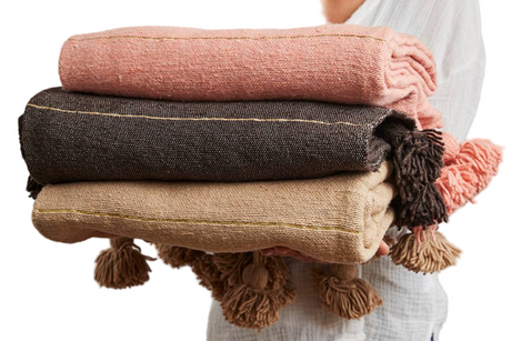 Person holding a stack of folded blankets in various colors.