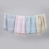Four scarves in gray, pink, blue, and beige hanging on a line against a gray background.