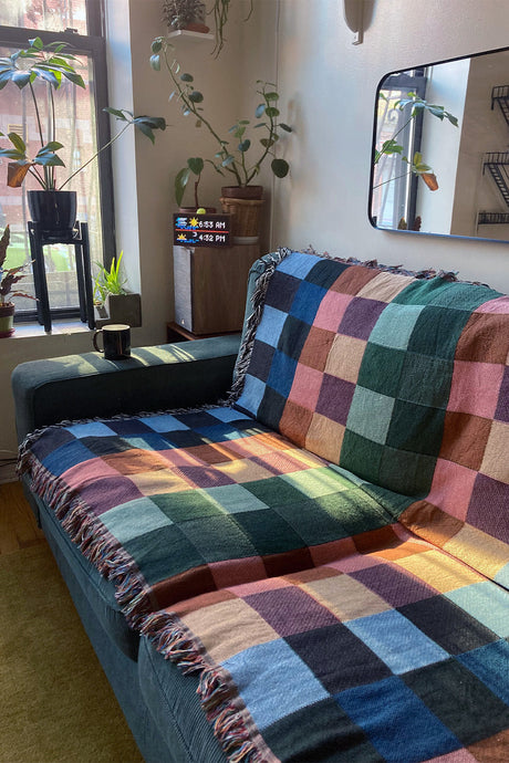 Vibrant checkered woven throw blanket draped over a couch, showcasing deep color tones and soft texture.
