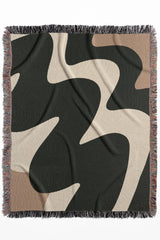 High-contrast cotton woven throw blanket featuring fluid shapes in black, off-white, and beige.
