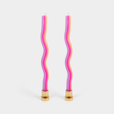 Two wavy, multicolored candles with gold bases on a light gray background