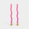 Two wavy, multicolored candles with gold bases on a light gray background