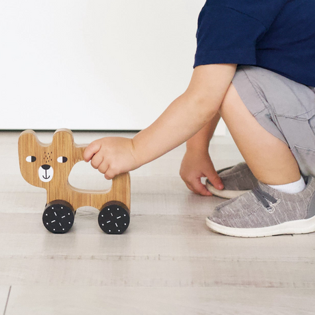 Child playing with a wooden bear toy on a light wooden floor.